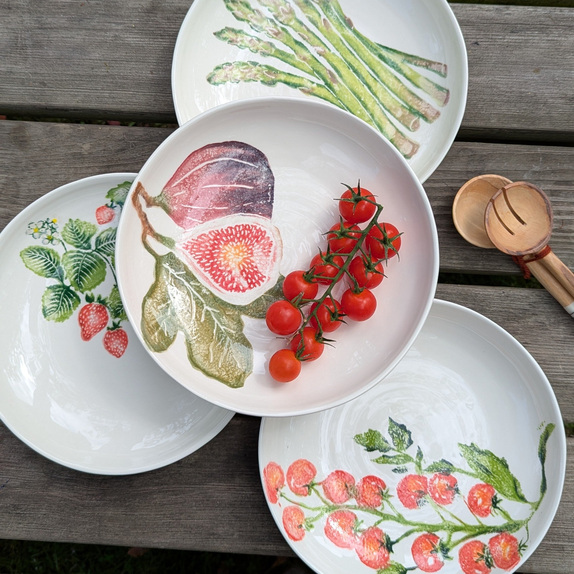 Set of white plates with fruit and vegetable illustrations on a wooden surface.