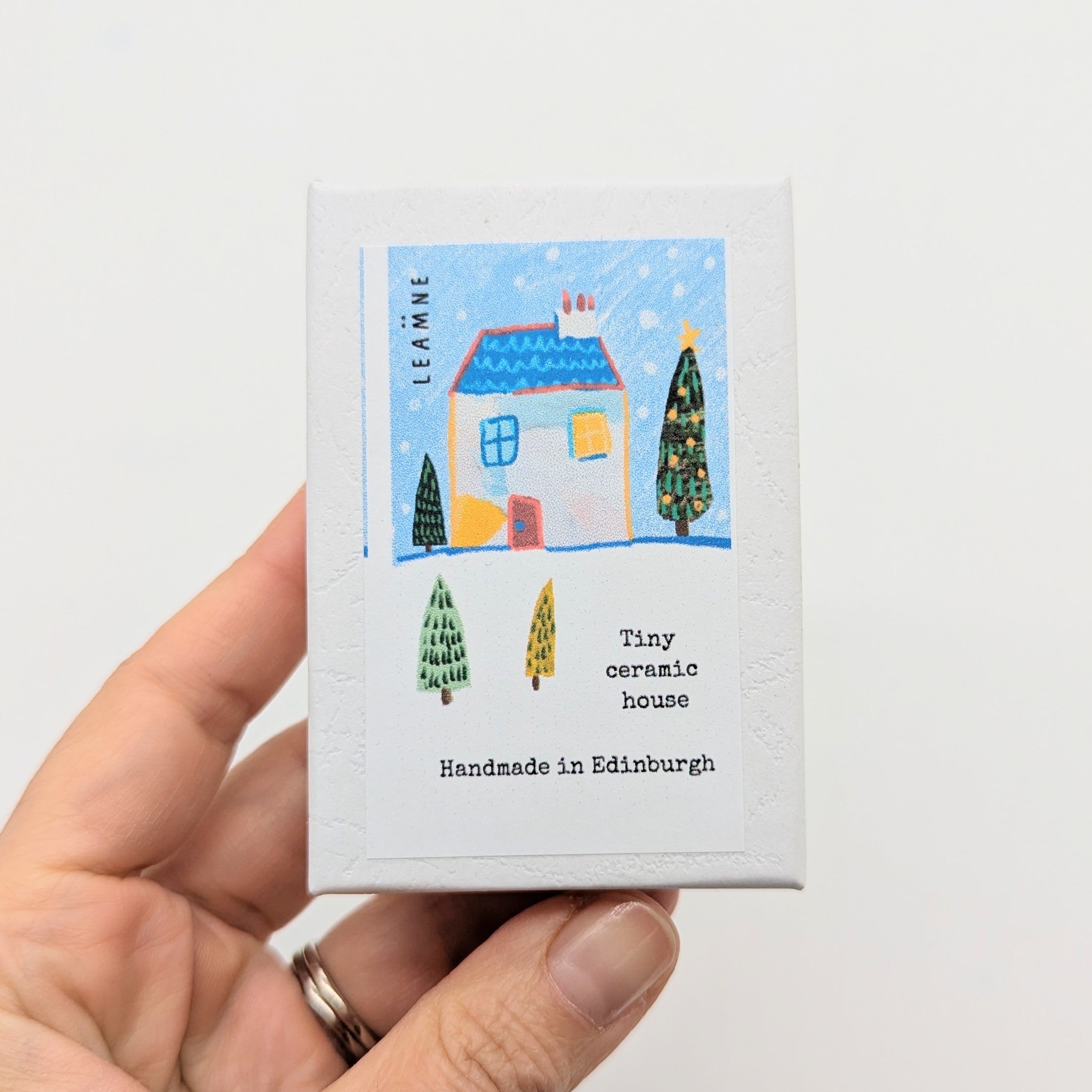 Hand holding a box with a miniature ceramic house design on a white background