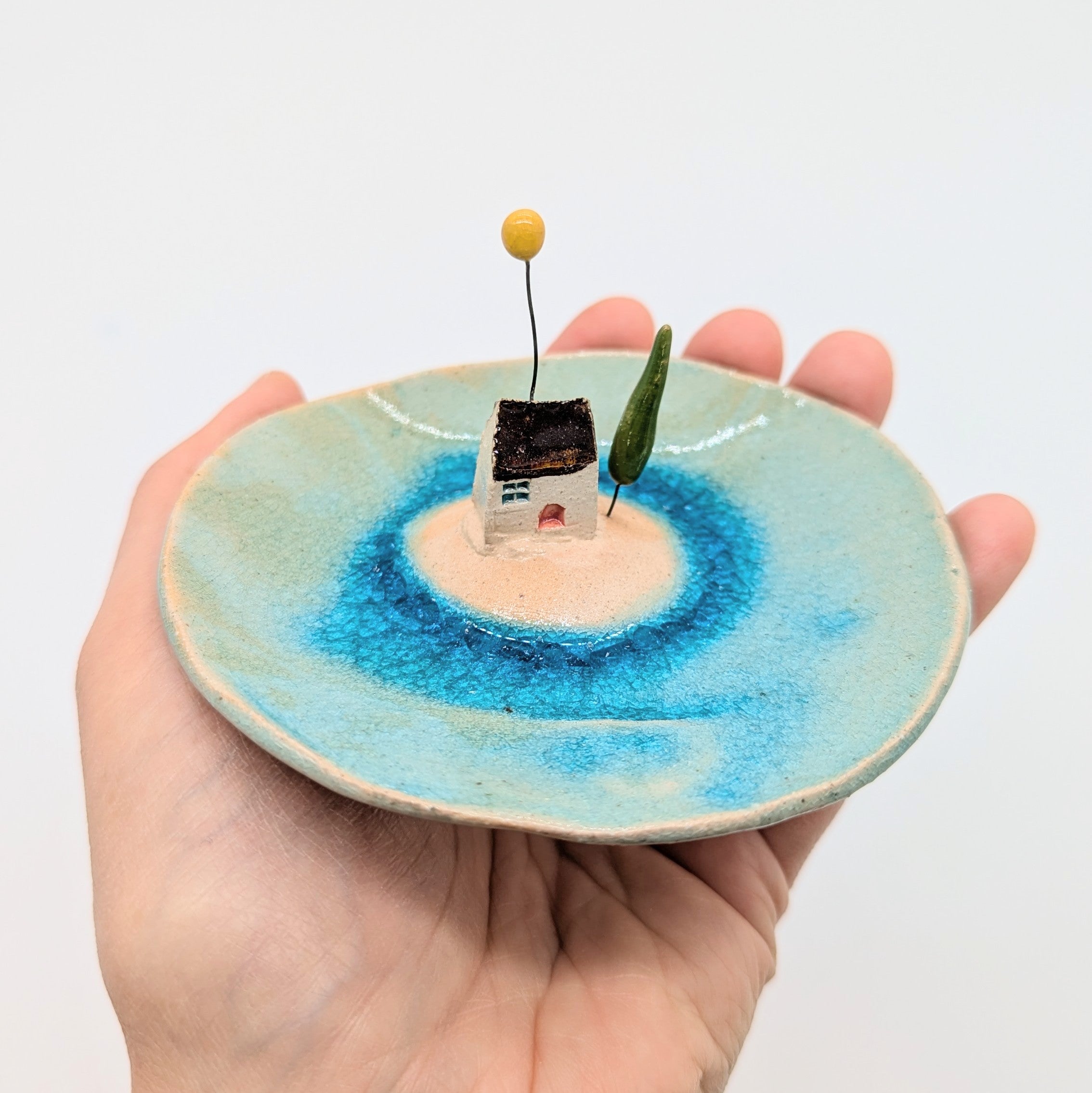 Hand holding a small ceramic dish with a miniature landscape on a plain background