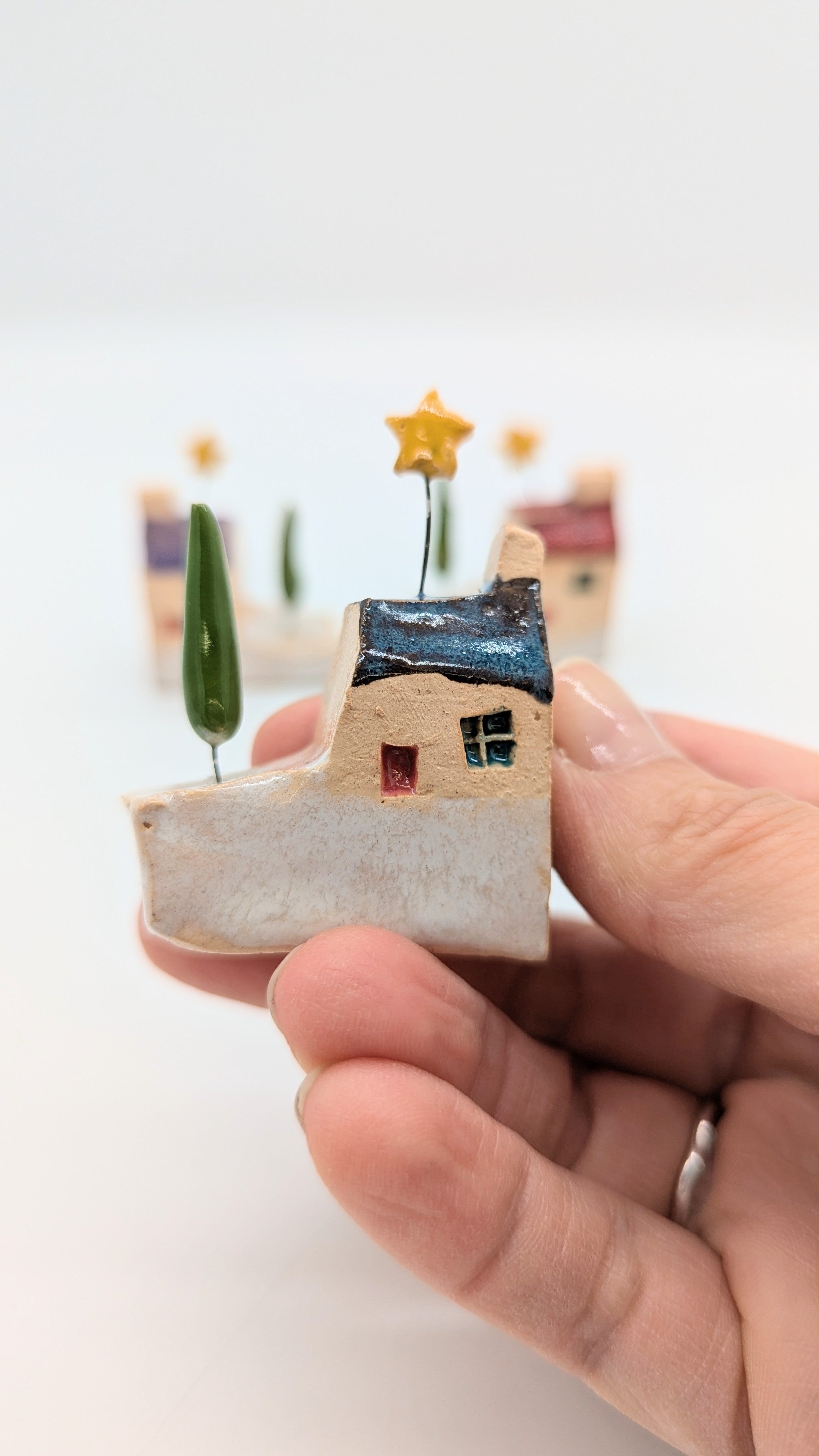 Hand holding a small decorative house with trees on a white background