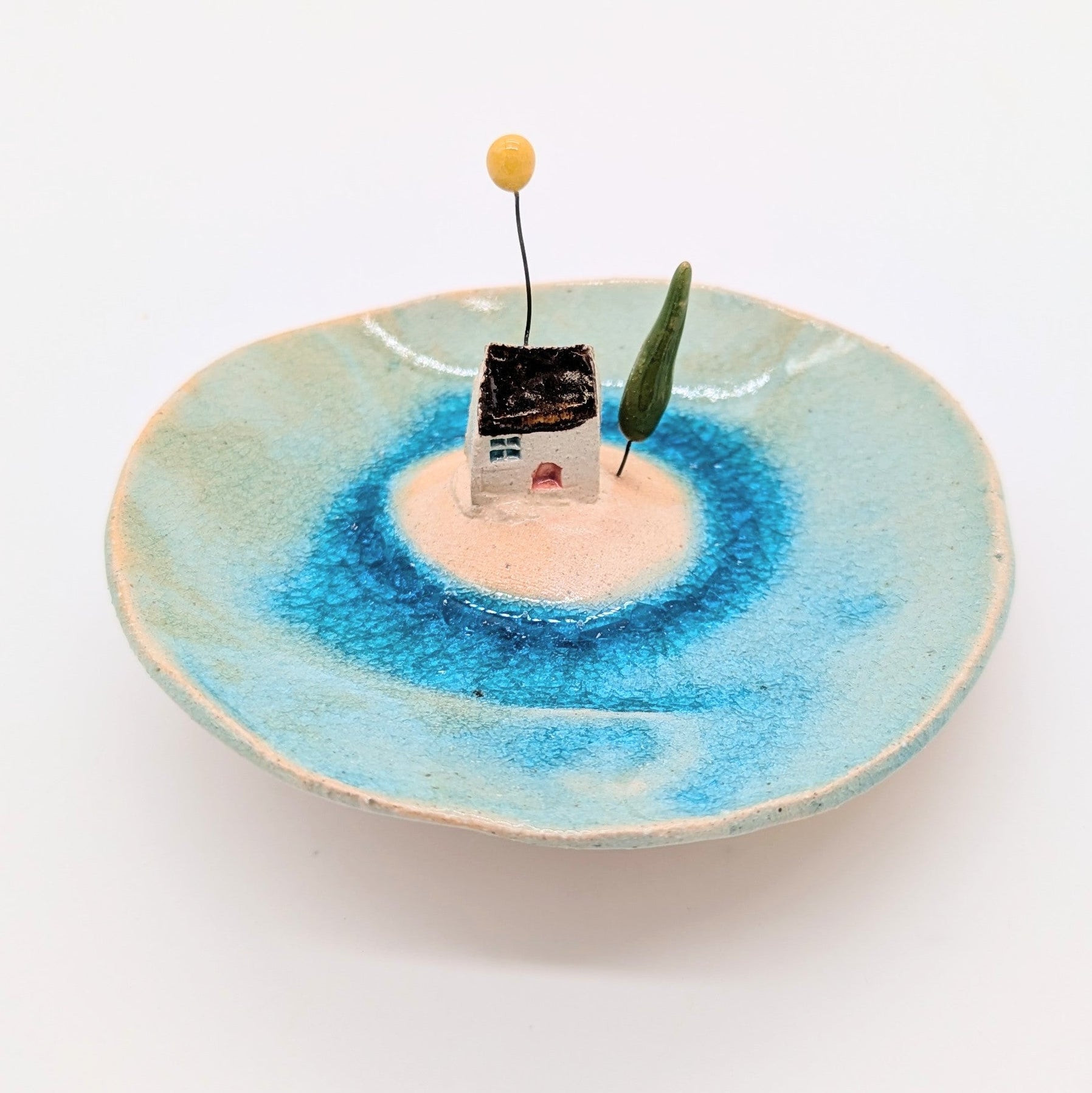 Ceramic dish with a small house sculpture on a white background