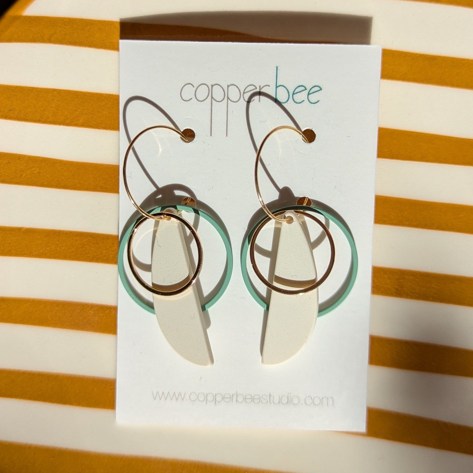 Copperbee earrings on a striped background