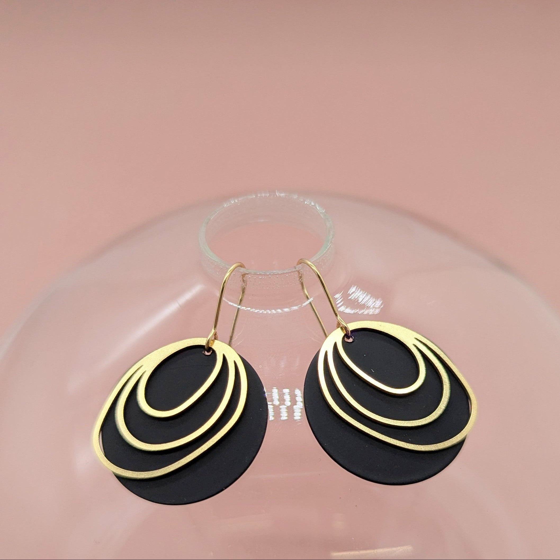 Black and gold earrings on a clear stand with a pink background