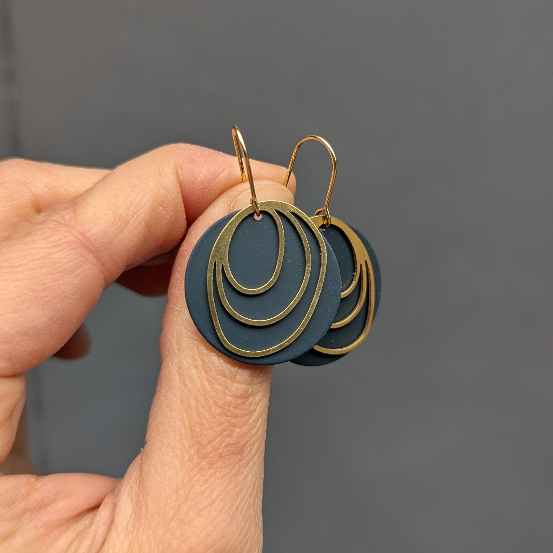 Hand holding a pair of earrings with concentric circles against a gray background