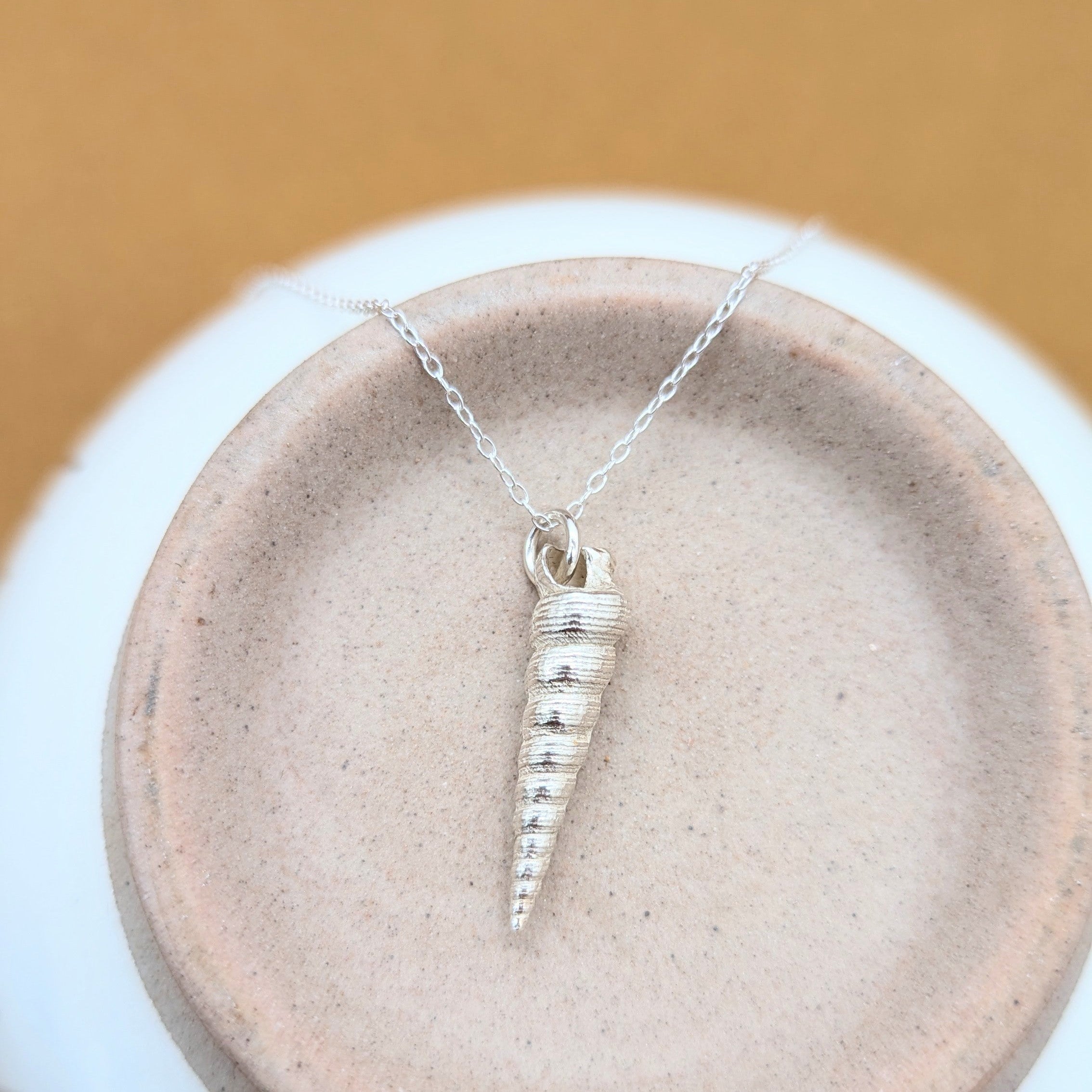 Silver shell necklace with a pendant on a white stand against a brown background
