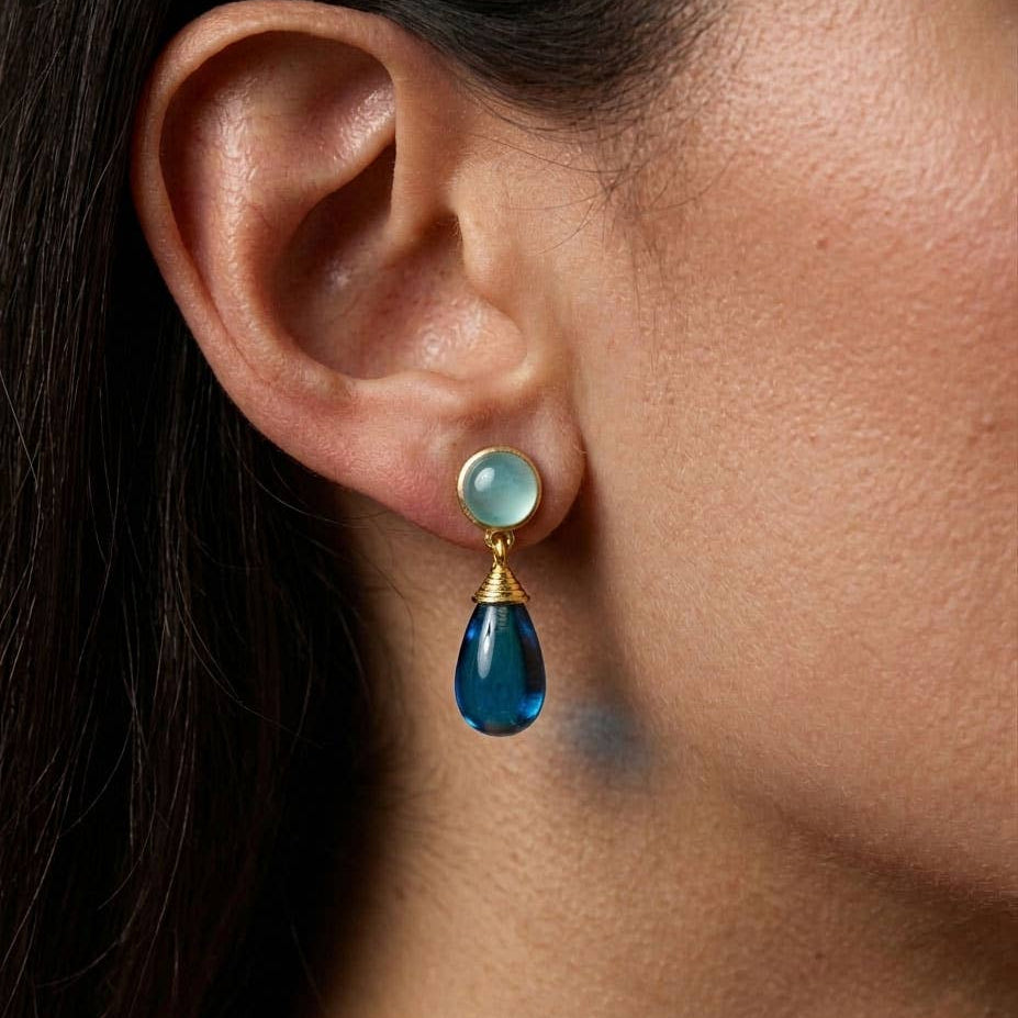 Close-up of an ear wearing a blue teardrop earring with a gold and aqua stone.