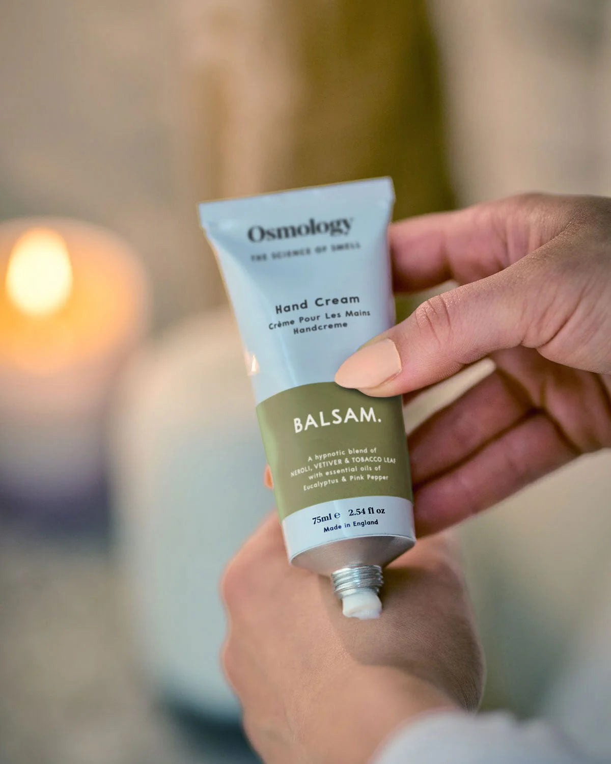 Hand holding a tube of Osmology Balsam hand cream with a blurred background