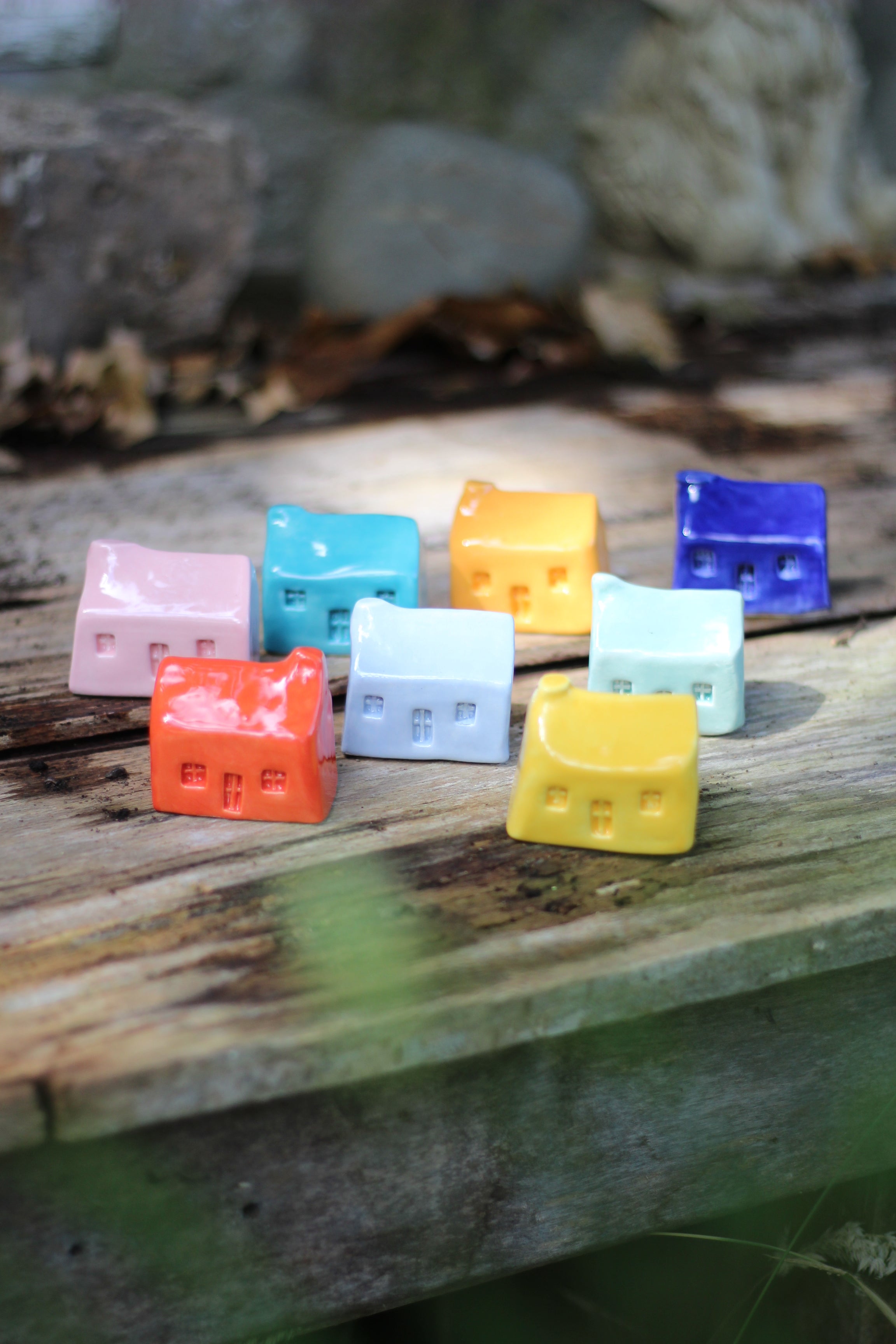 Eight small ceramic houses in block colours tanding on aged wooden surface in natural light