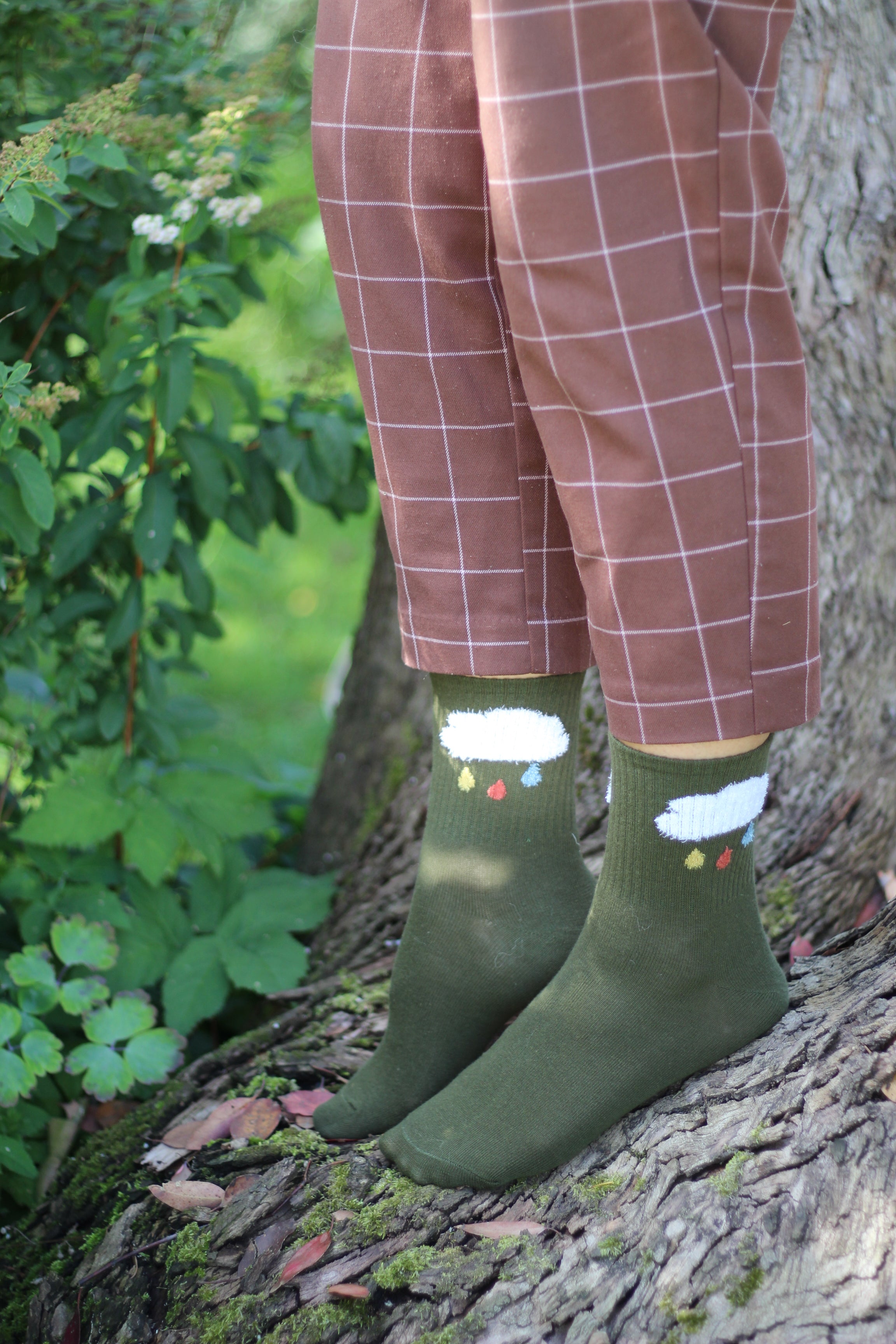 Person wearing green socks with white rain clouds standing on a tree trunk.
