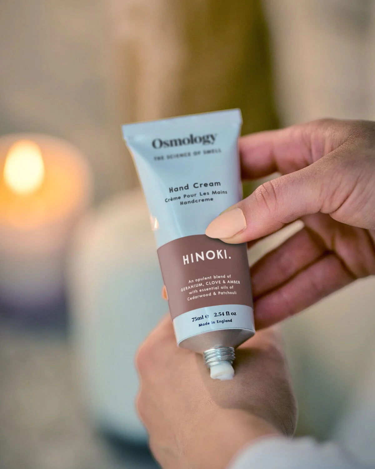 Hand holding a tube of Osmology Hinoki hand cream with a blurred background