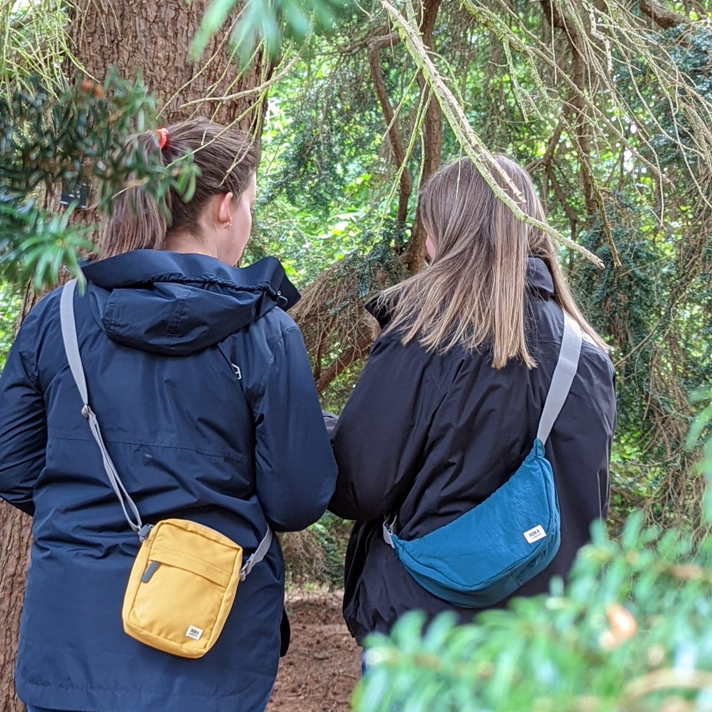 Two people n the woods facing away from the camera wearing Roka bags