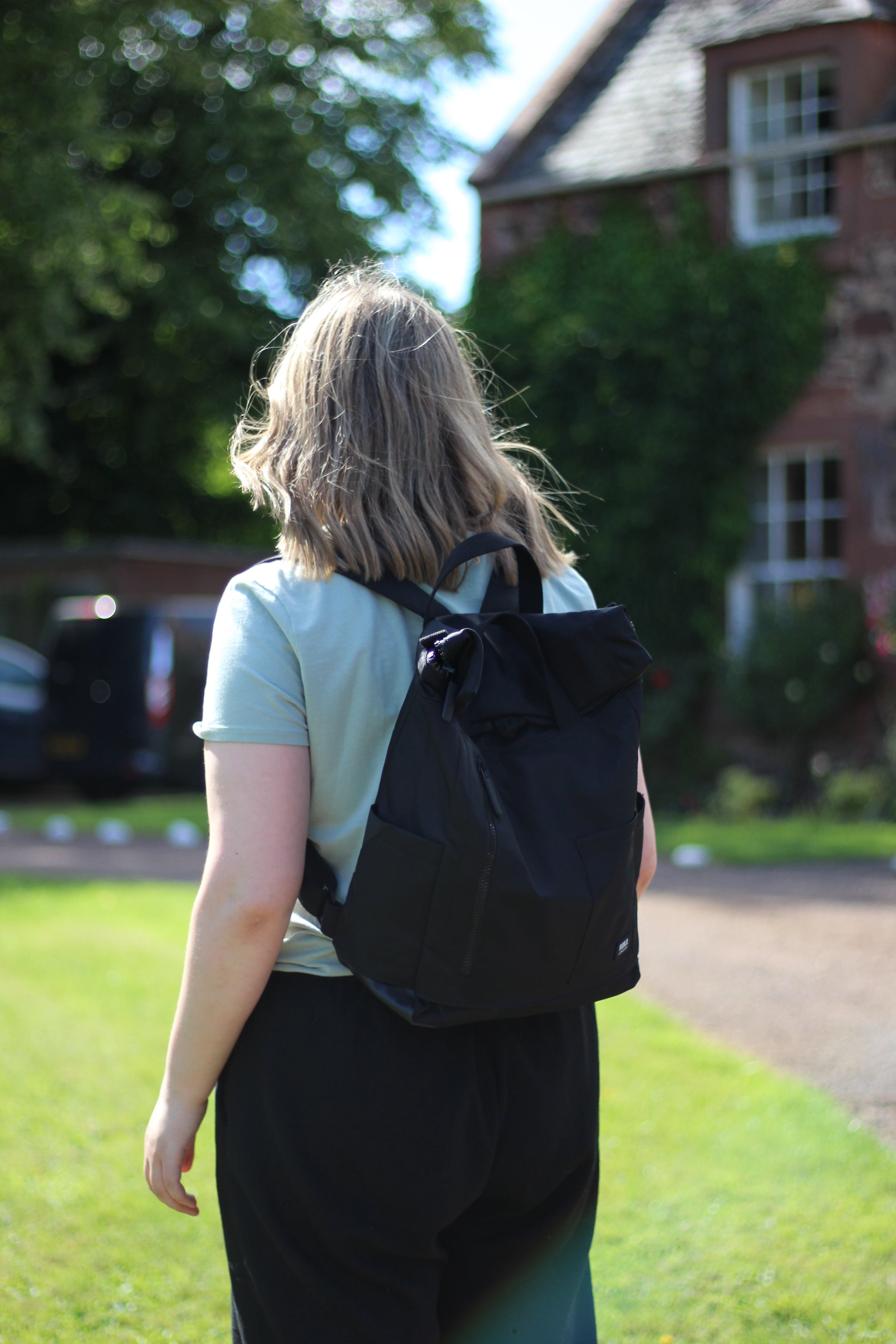 Person wearing a black Recycled backpack outdoors on a nice day.
