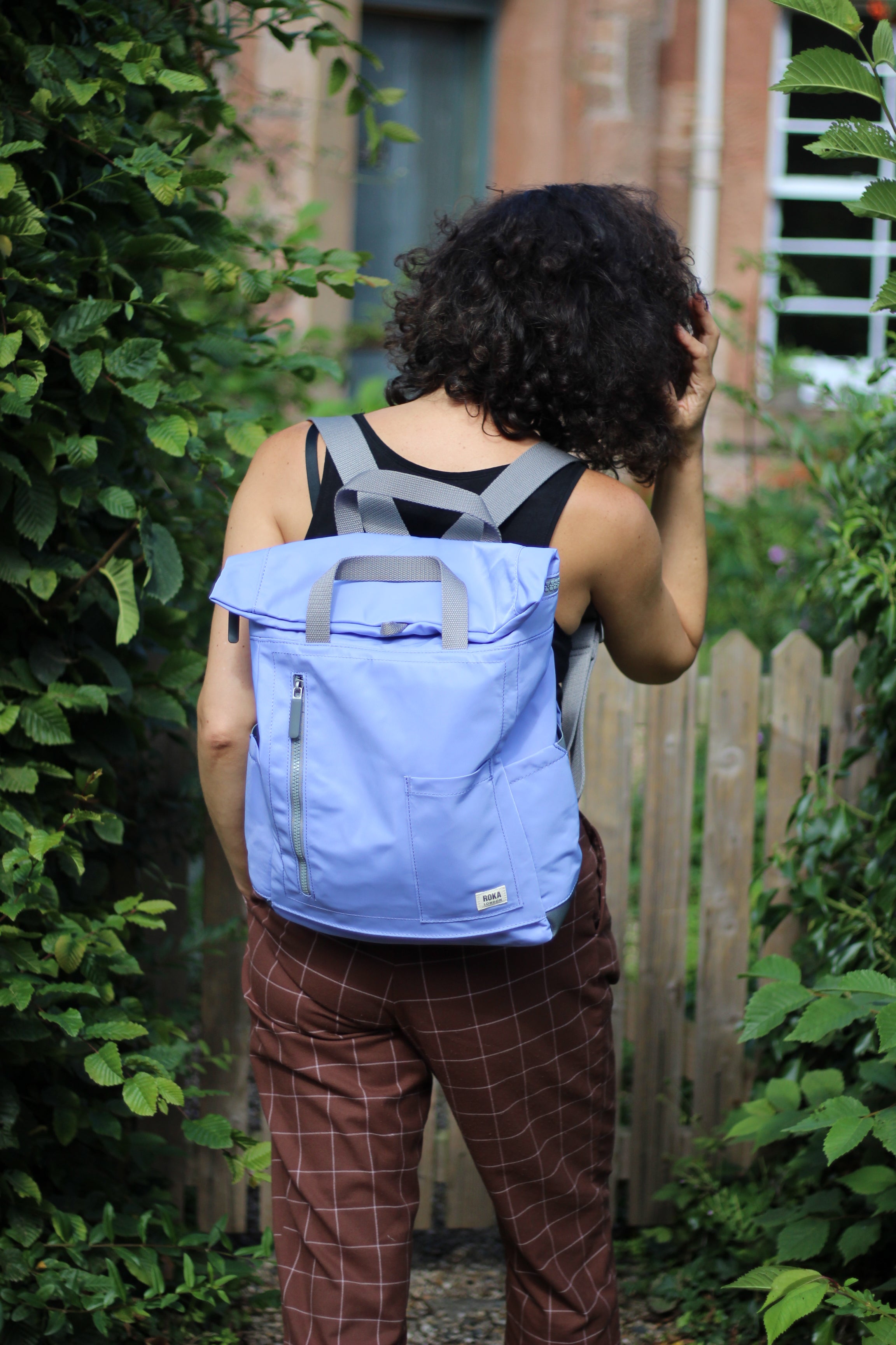 Person wearing a lilac backpack outdoors with greenery and wooden fence in the background