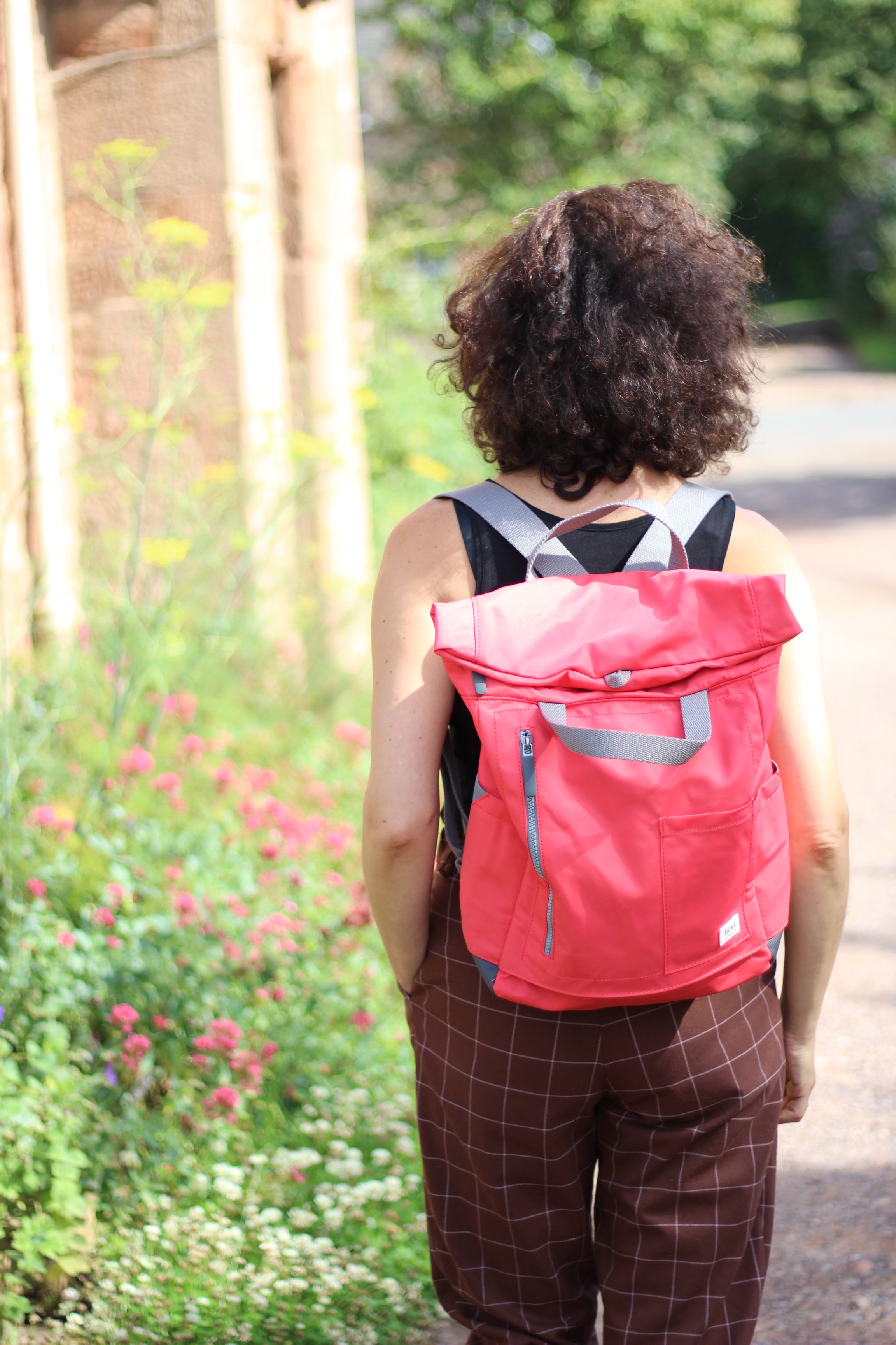 Person wearing a bright pink backpack outdoors with greenery in the background.