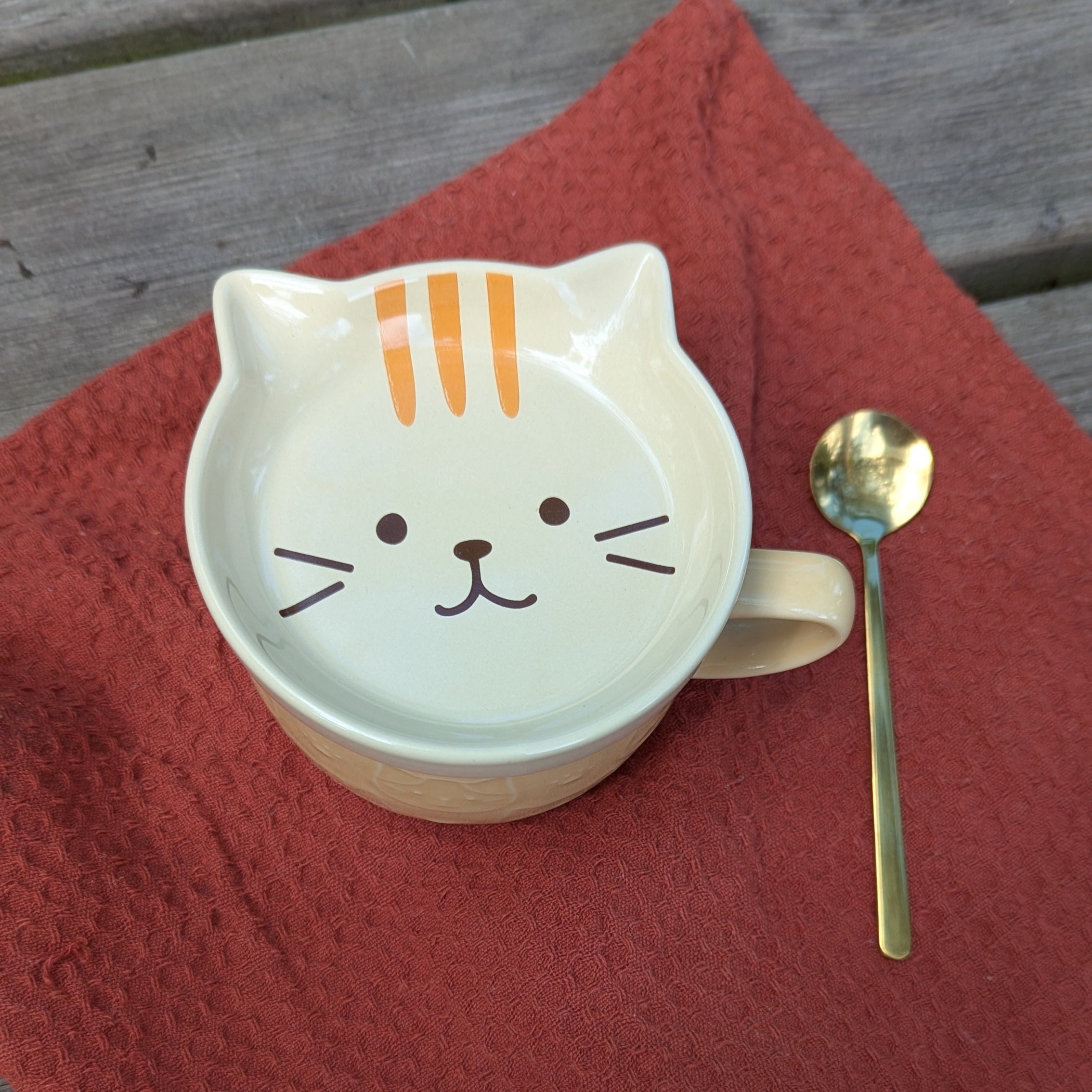 Cat-shaped ceramic saucer and mug with a spoon on a red cloth