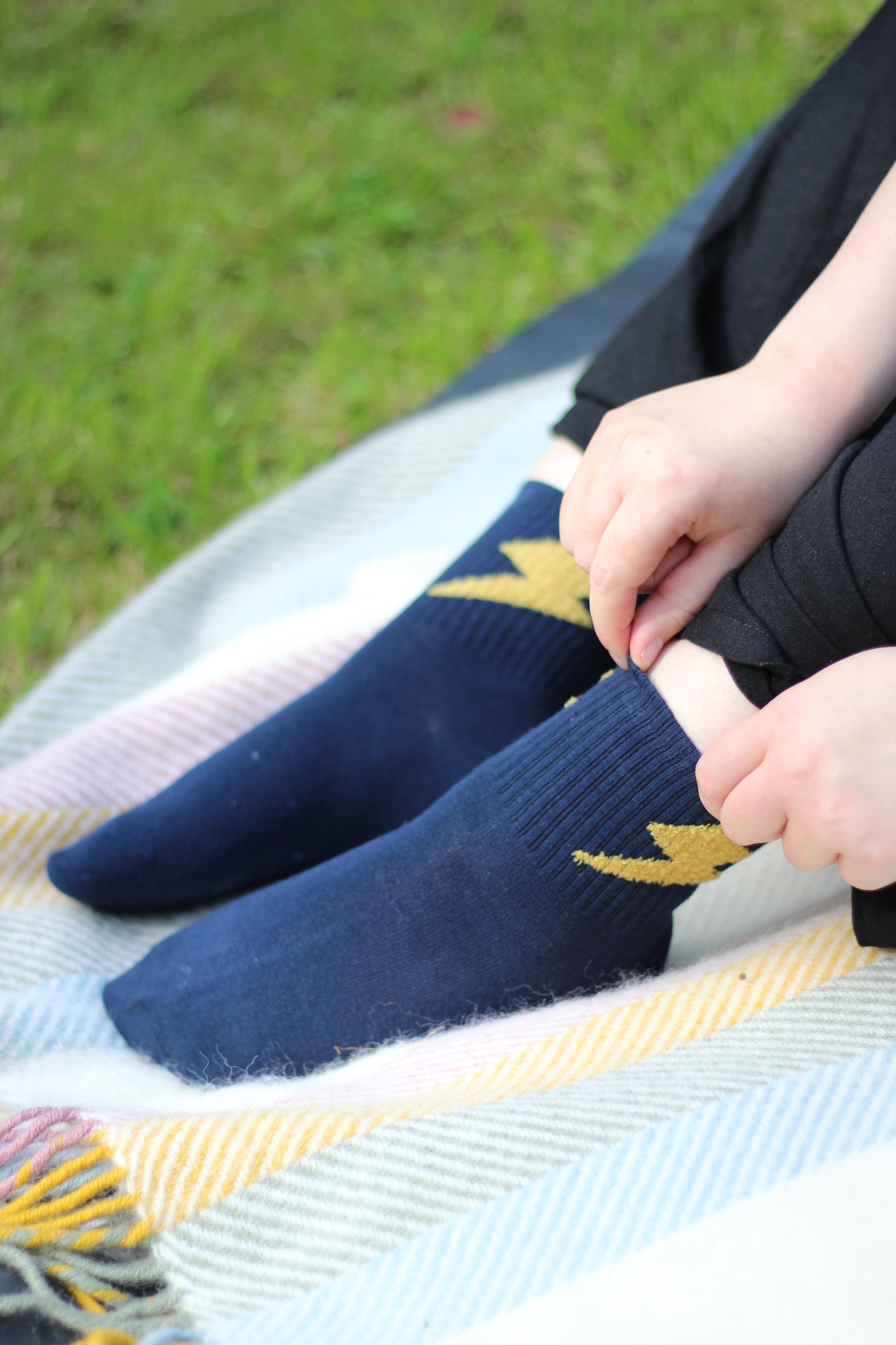 Person wearing dark blue socks with a lightning bolt pattern, sitting on a blanket.