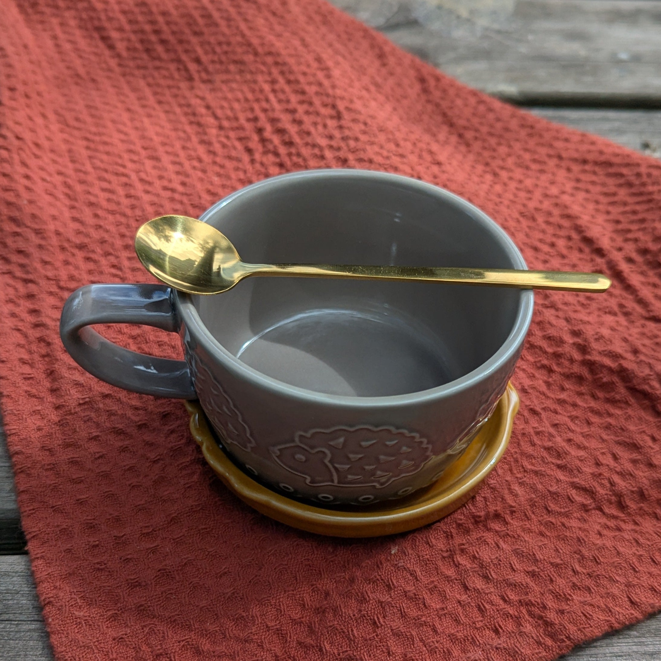 Gray mug with a gold spoon on a red cloth on a wooden surface