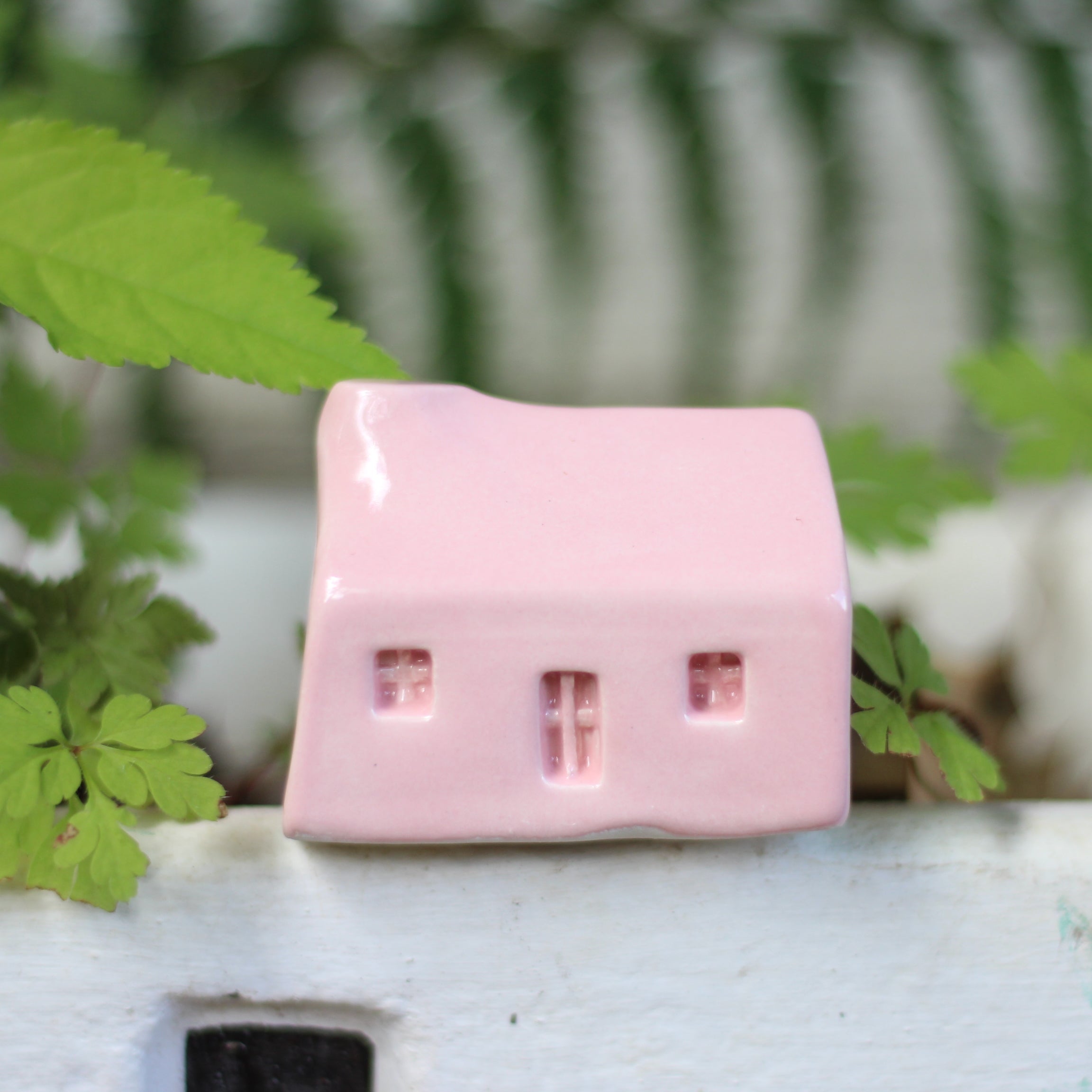 Pink ceramic house on a white surface with green leaves in the background