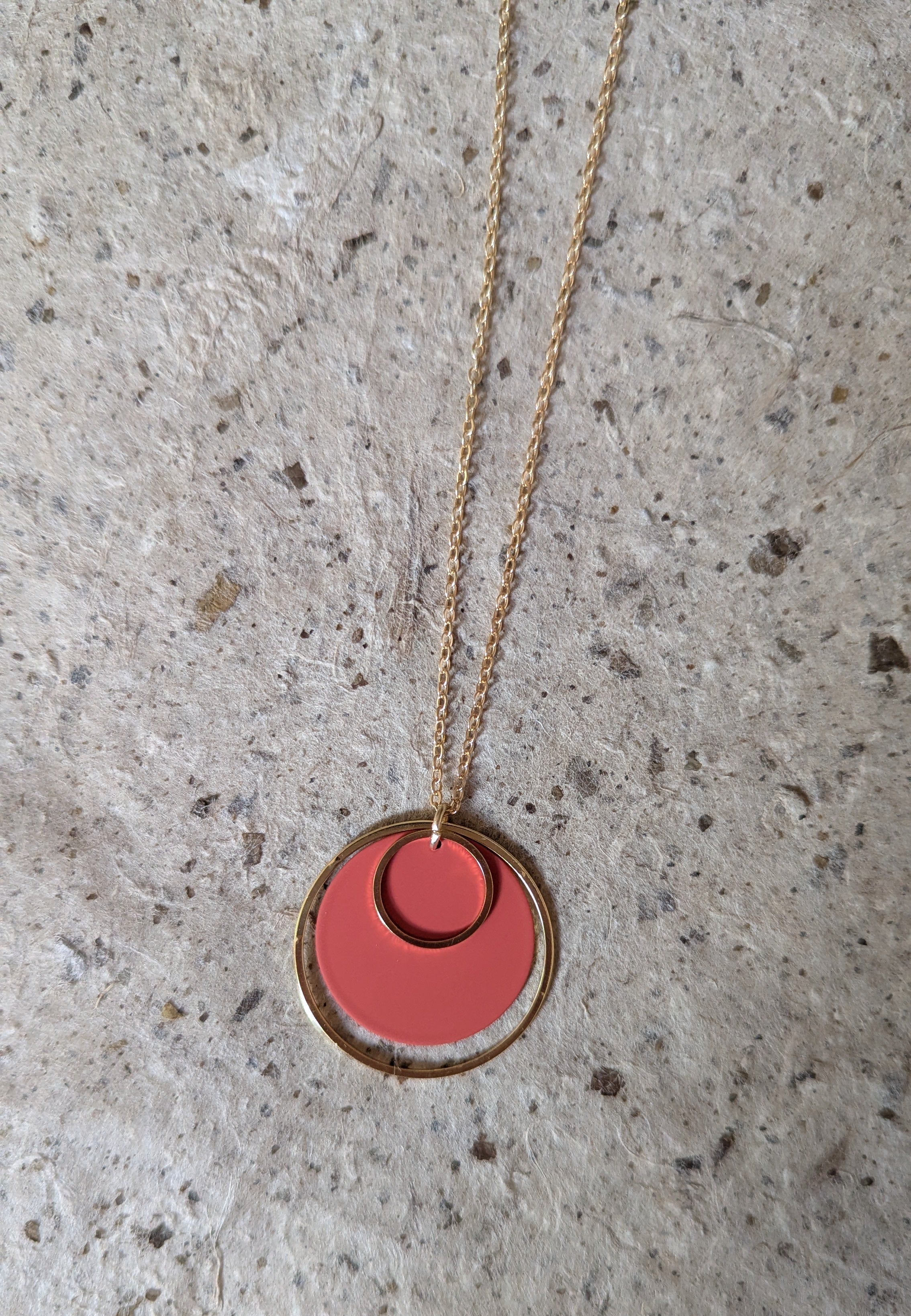 Necklace with a rust orange pendant on a textured gray surface