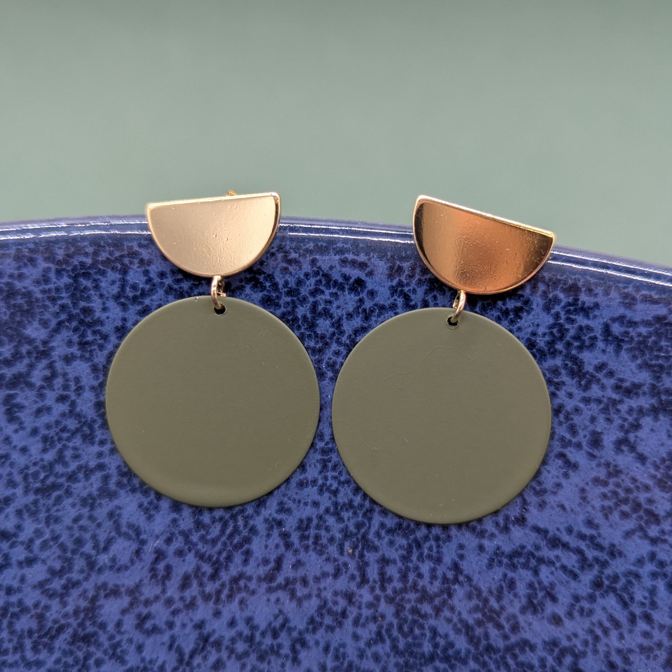 Gold and green earrings on a textured blue surface