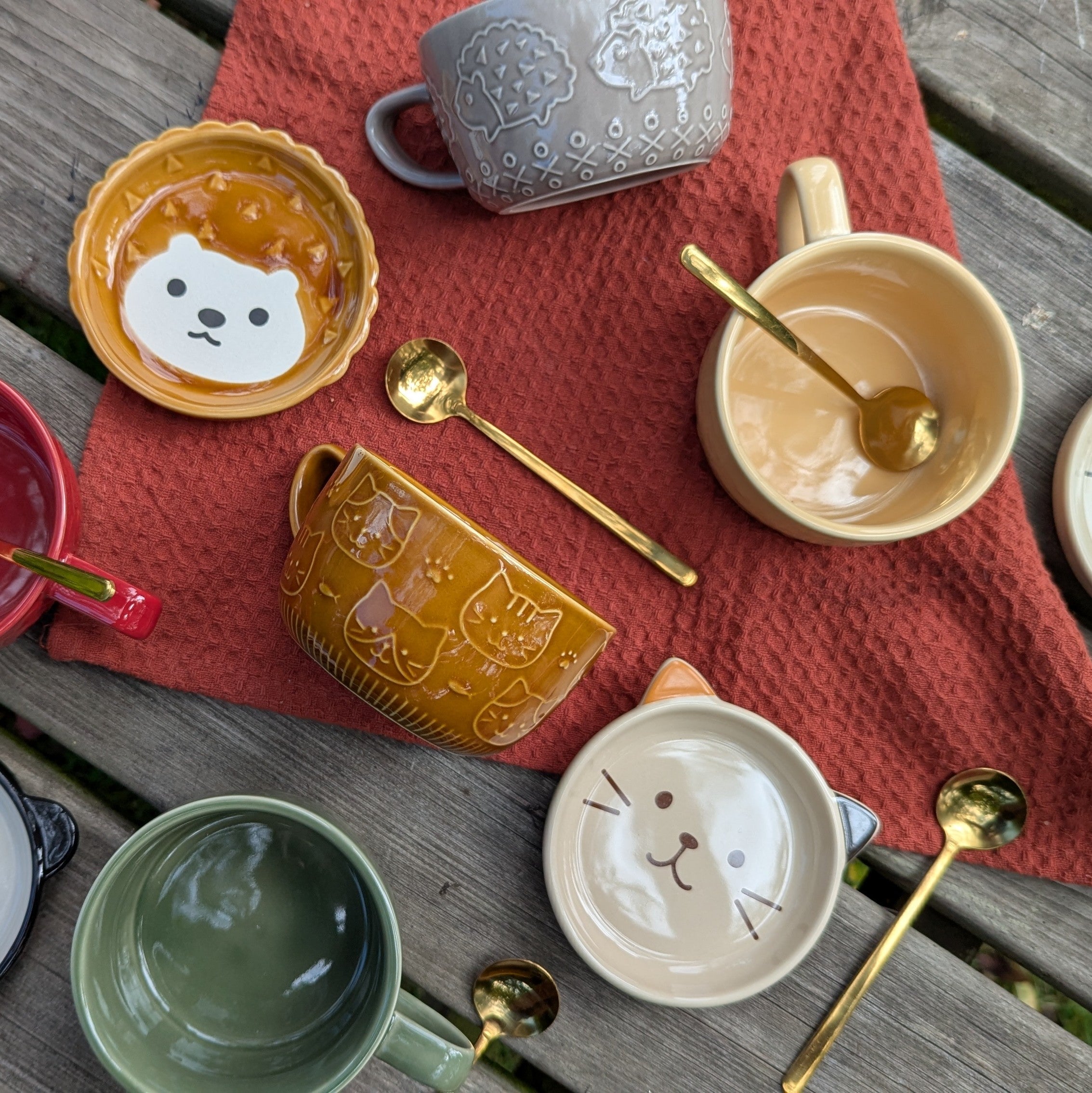 Collection of ceramic bowls and mugs with animal designs on a wooden table.